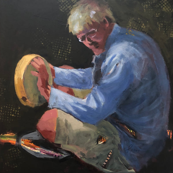 A man with blonde hair and glasses, wearing a long sleeved blue shirt, taps out a rhythm on a hand drum.