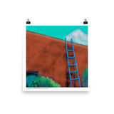 Blue handmade ladder leaning against an adobe wall with shrubs below and turquoise sky above. By Laura Hunt.